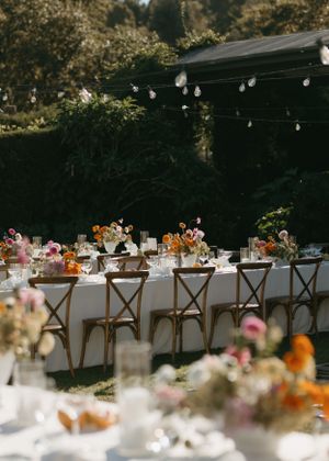 Elegant outdoor wedding reception setup with wooden cross-back chairs and string lights overhead.