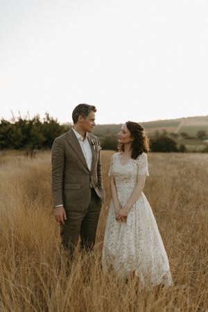 A couple shares a romantic moment in a golden field at sunset wearing wedding attire.