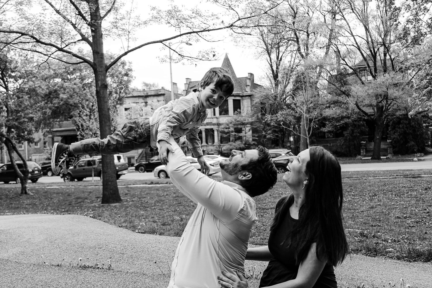 Two people playfully interact outdoors with a historic house visible in the background.