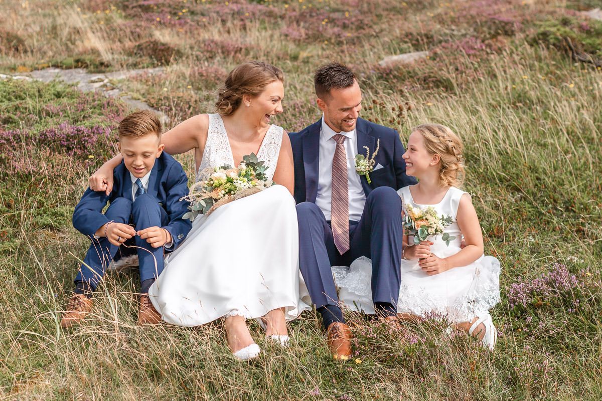 Brudeparet og deres to barn sitter sammen i lyngen på Solastranden.