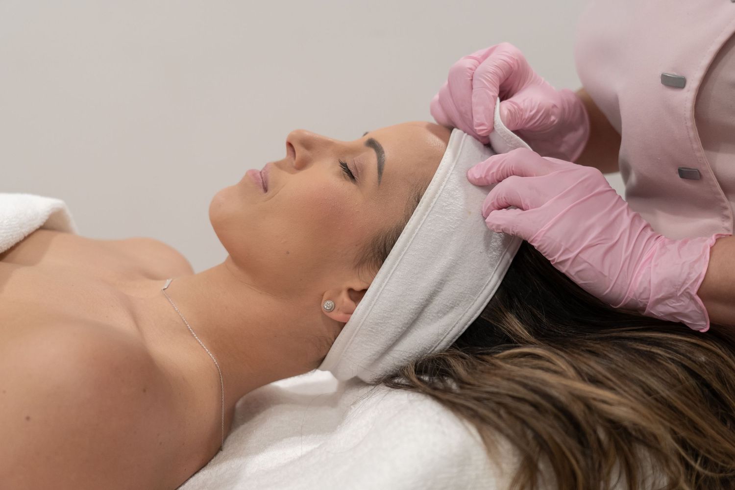 Esthetician wearing pink gloves performs facial treatment on relaxed client at spa.