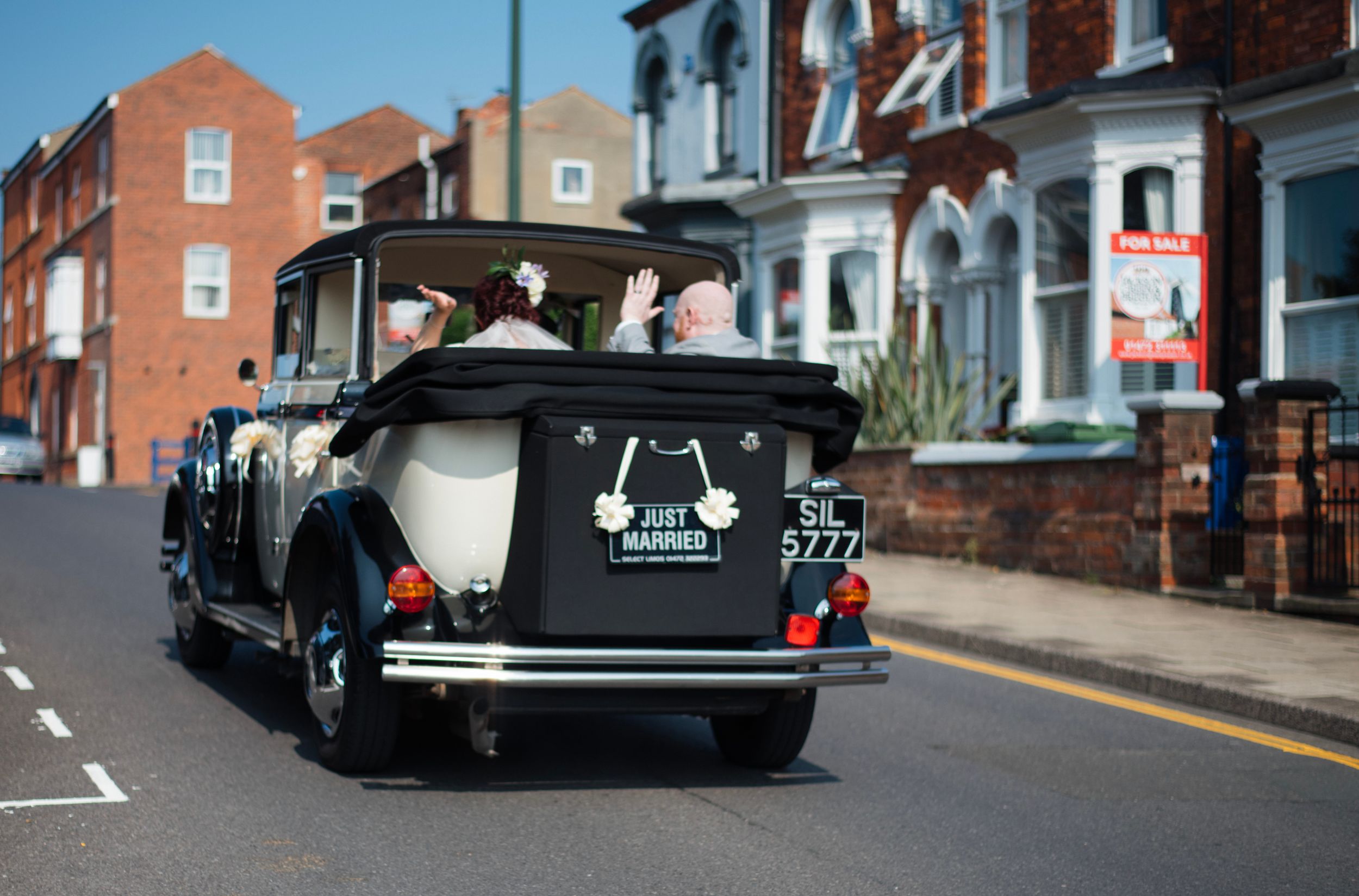 Vintage wedding car with decorative signage viewed from behind on urban street.