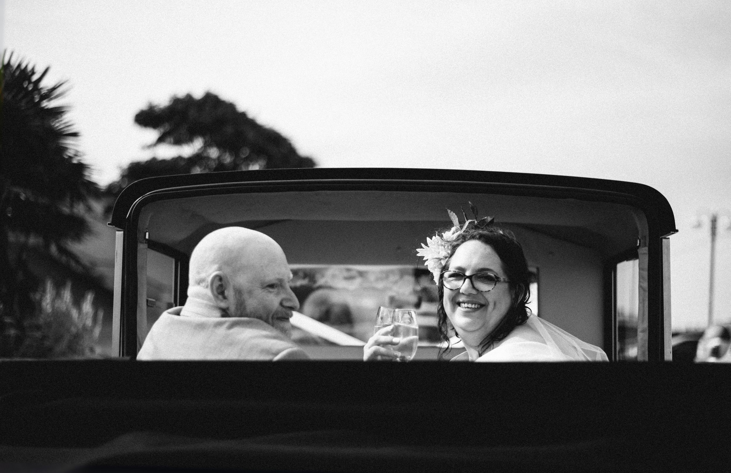 Black and white photo of newlyweds sharing a moment in vintage car.