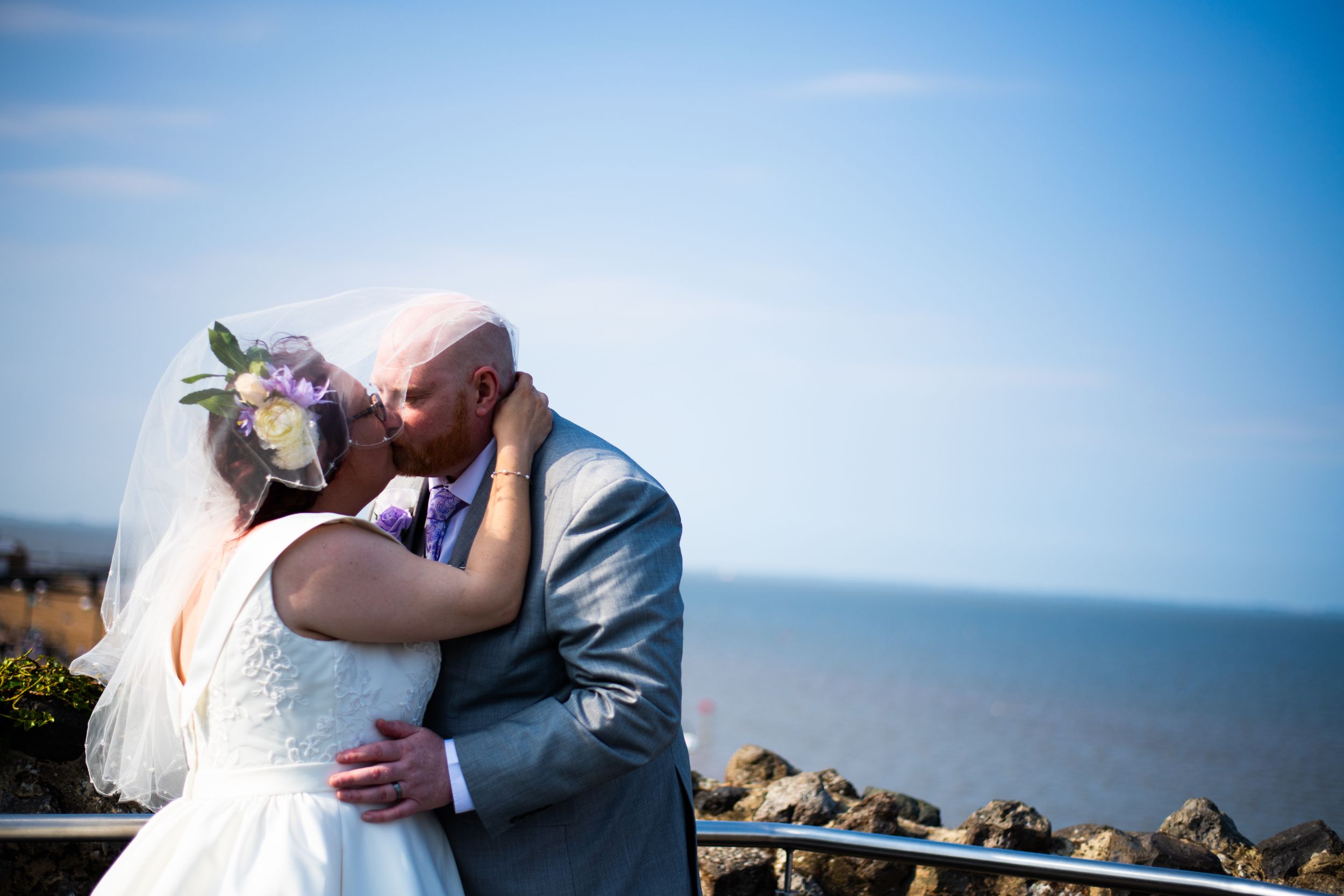 Intimate wedding kiss on oceanside terrace with blue sky backdrop.