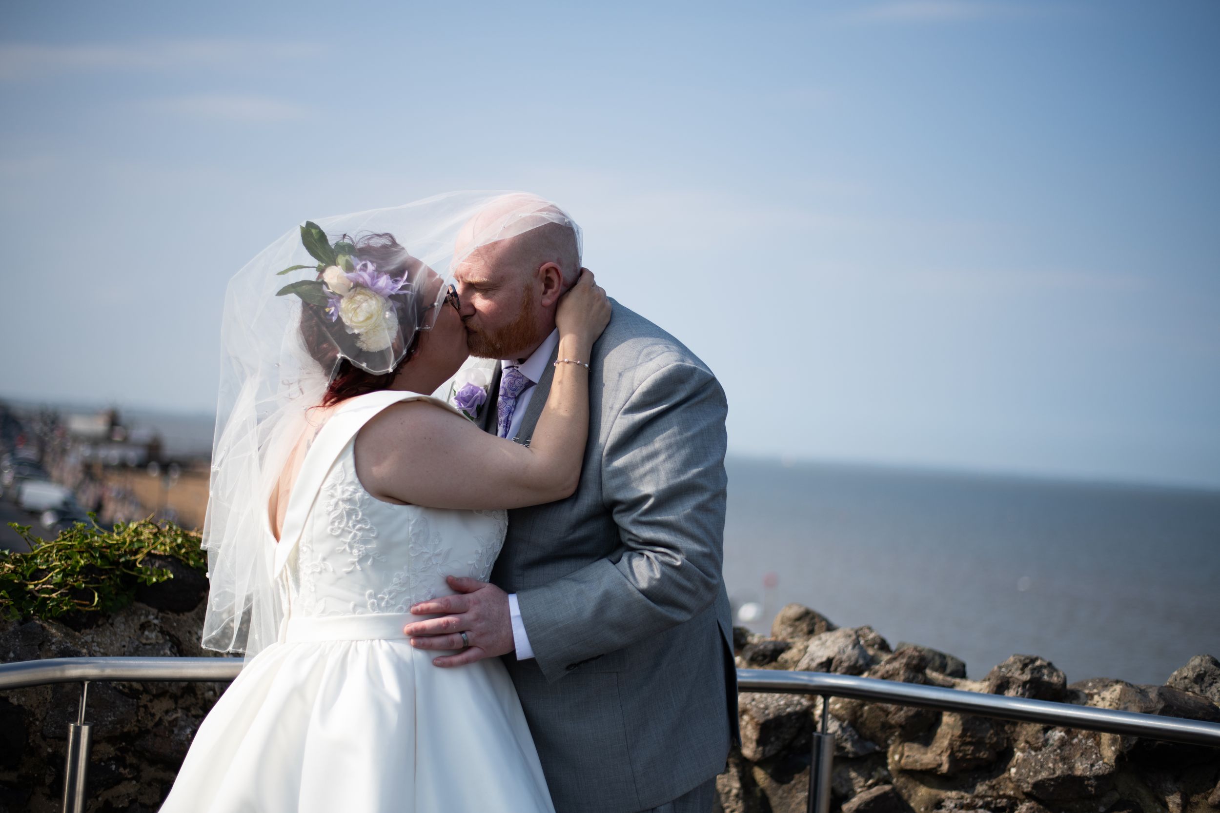 Romantic wedding embrace against bright blue sky and ocean view.