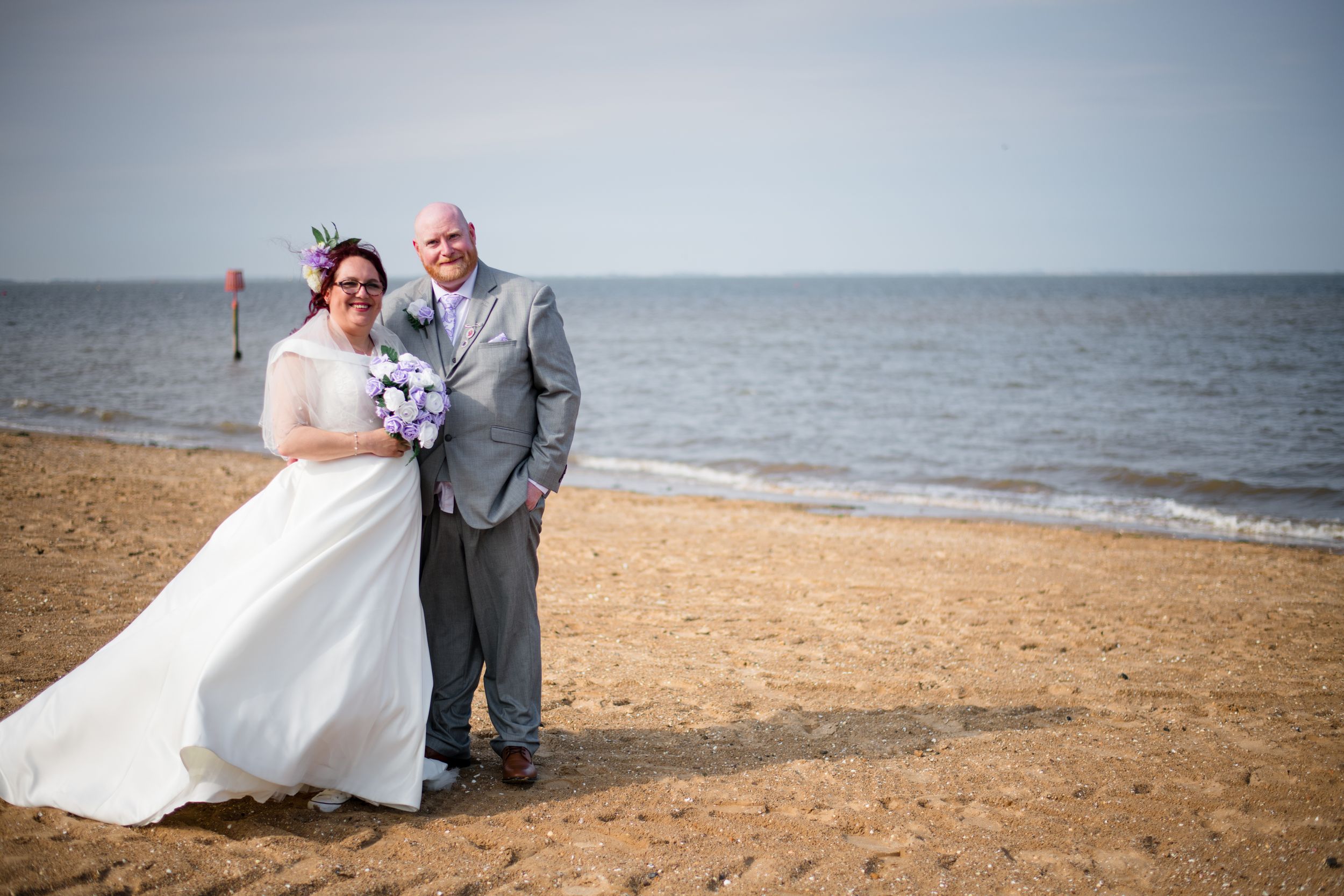 Wedding couple standing together on beach with ocean backdrop.