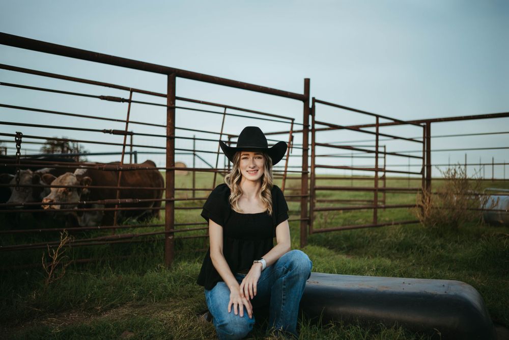 Black dress and cowboy hat against a ranch backdrop with metal gates.