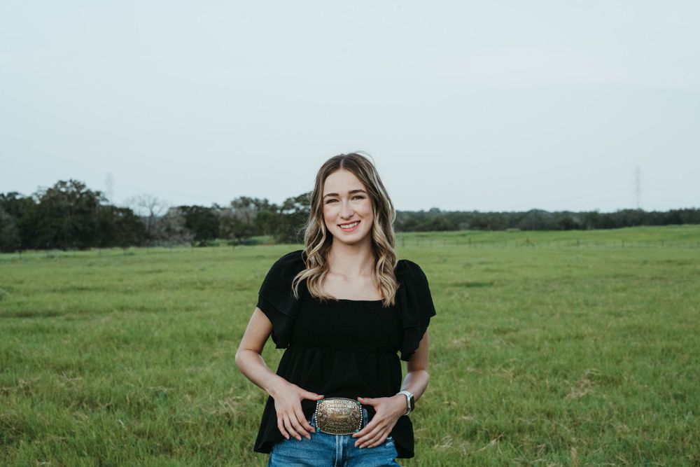 Western style outfit with belt buckle against green pasture landscape.