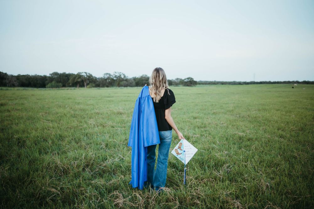 A figure wearing a blue cape stands in a green pasture holding a sign against a cloudy sky.
