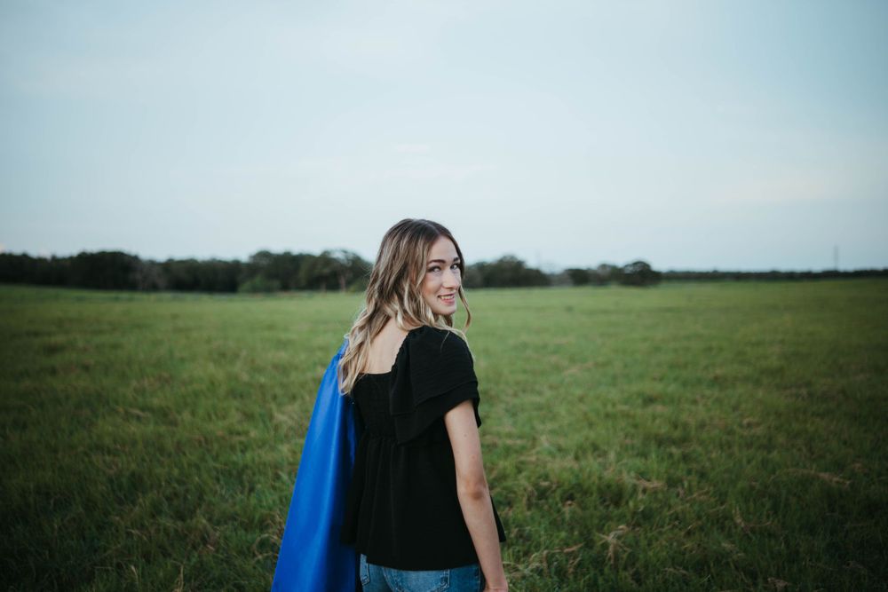 Figure in black shirt and blue jacket walking through green pasture.