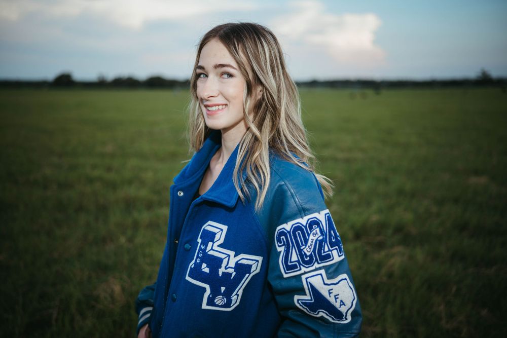 Letterman jacket with school emblems shown against pastoral background.