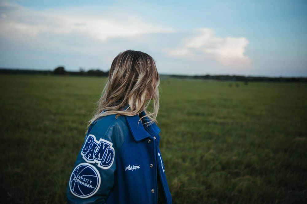 Blue letterman jacket with patches shown from behind in field.