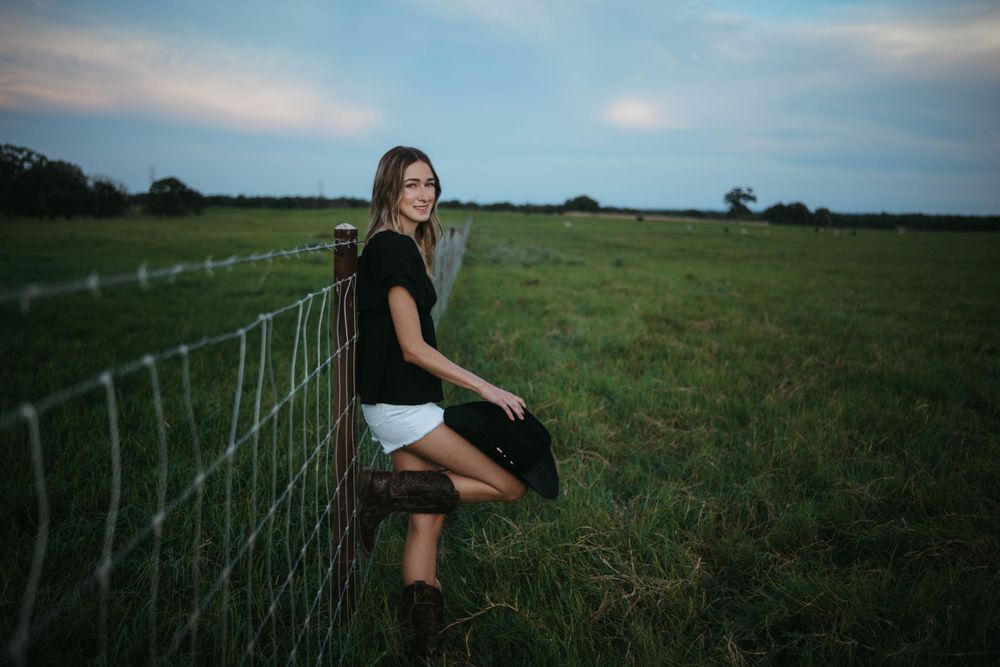 Black dress and boots perched on wire fence at dusk.