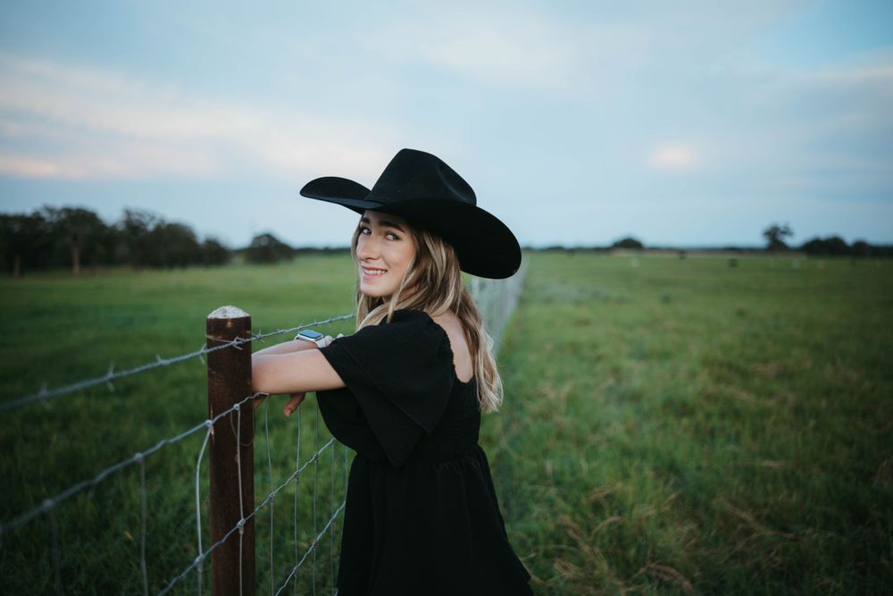 Black cowboy hat and dress silhouetted against fence at dusk.