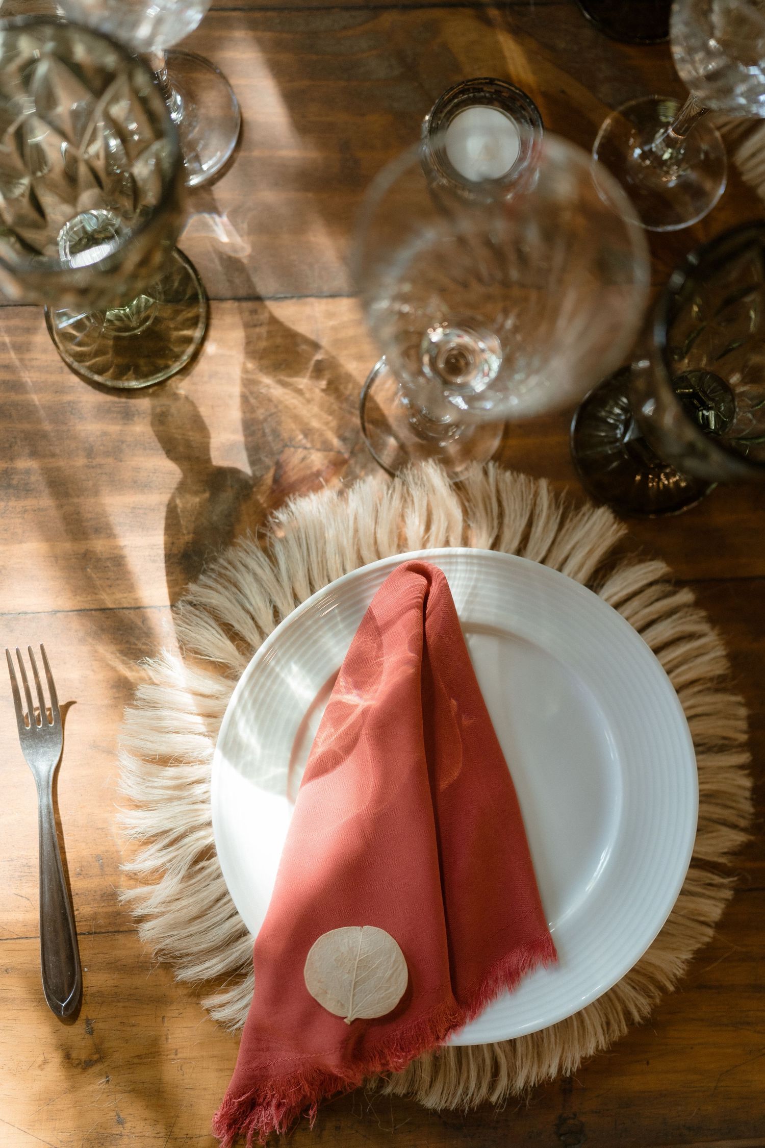 Place setting with coral napkin on textured charger plate with wine glasses.