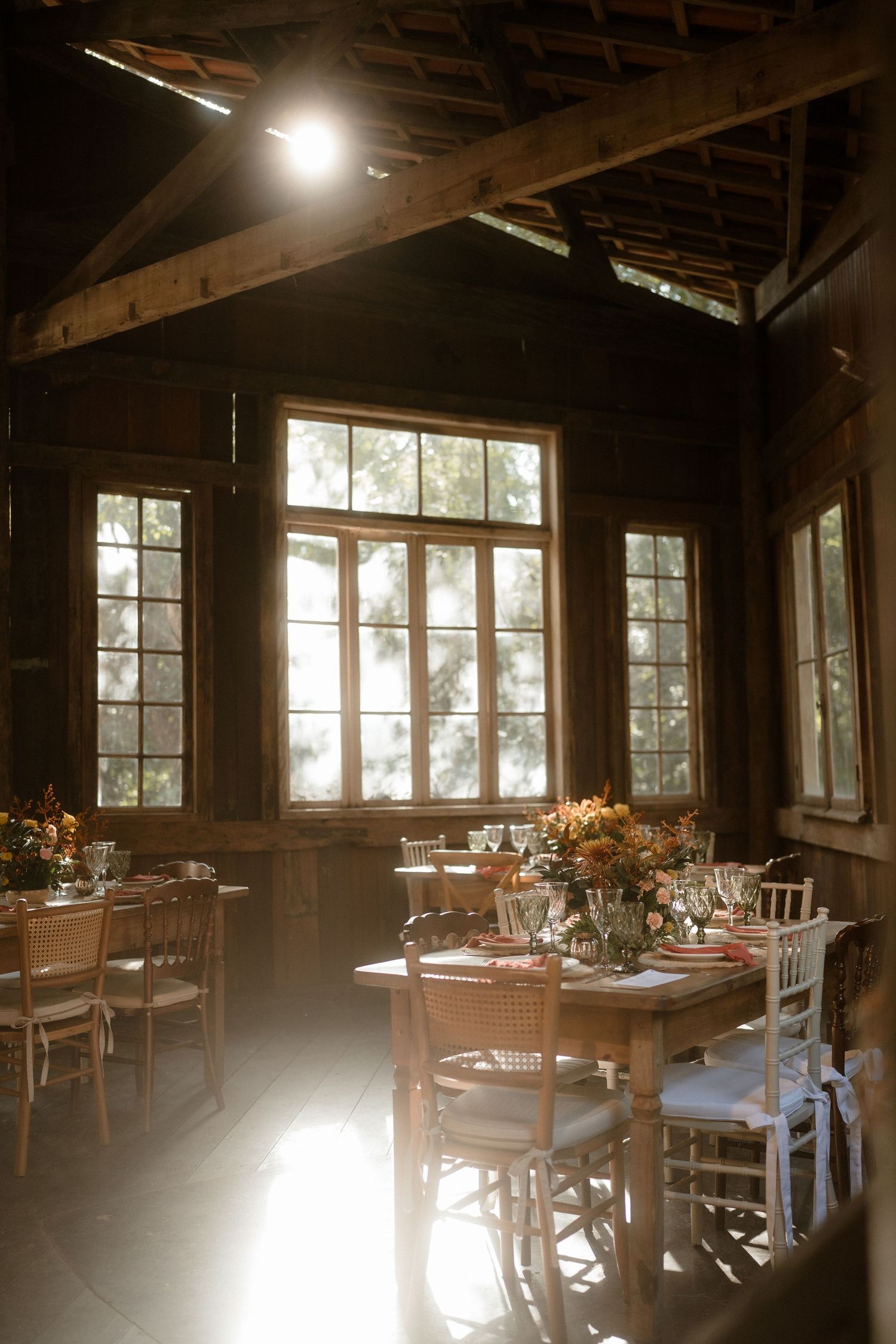 Sun-filled rustic dining room with wooden tables set for an elegant event.