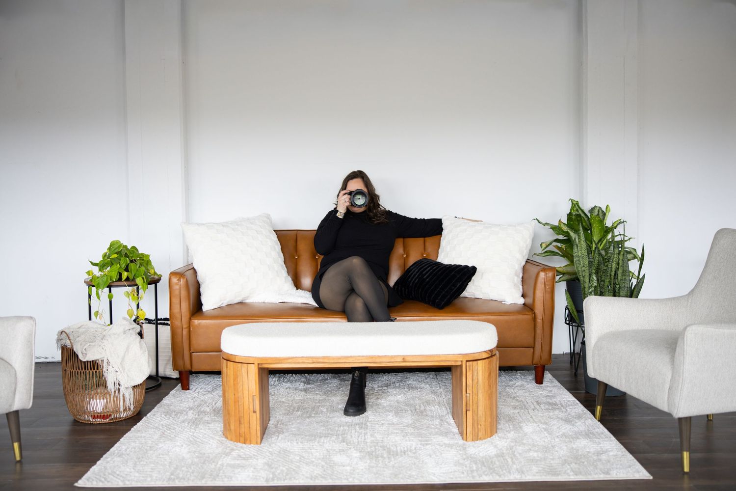 Woman relaxing on leather sofa with laptop in bright modern living room with indoor plants.