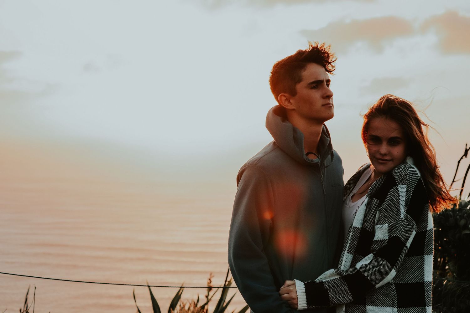 Couple in warm clothing embracing during sunset against coastal backdrop. Auckland Wedding Photographer and videographer