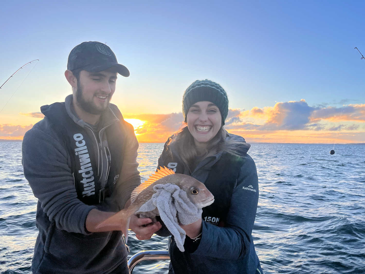Two people holding caught fish on boat during sunset over ocean.