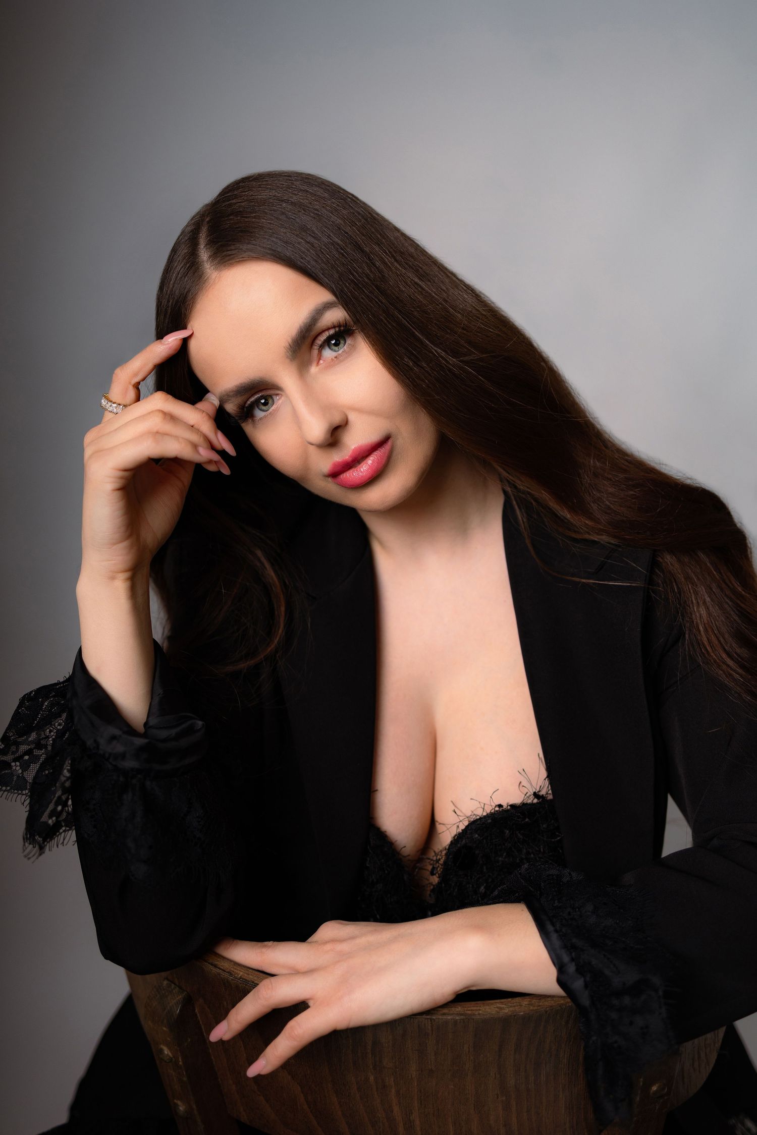 Elegantná brunetka v čiernom čipkovanom saku s hlbokým výstrihom a ružovým rúžom, štúdiový portrét. Žilina.