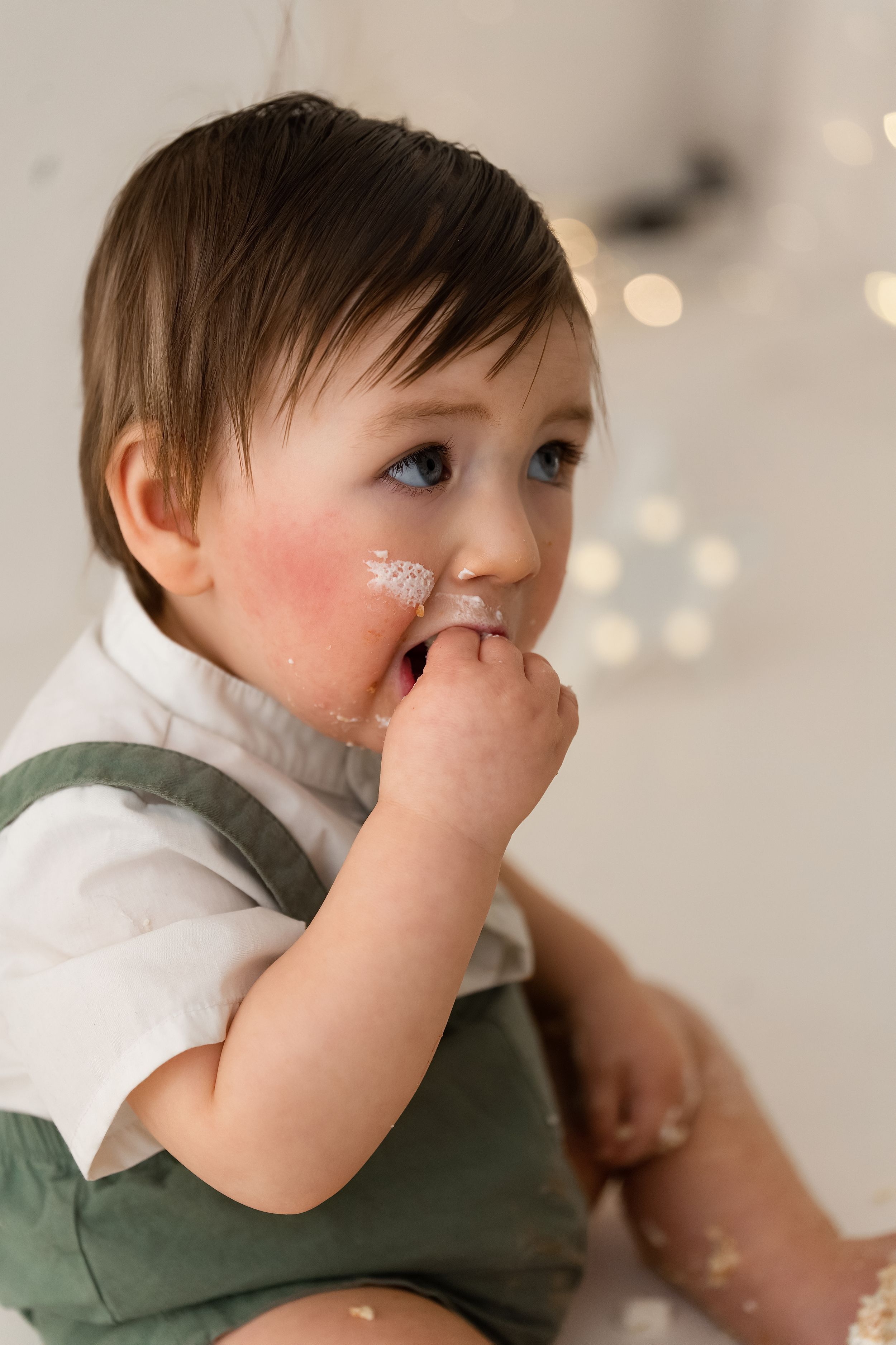 Adorable baby boy with blue eyes and cake frosting on his face during a first birthday cake smash.