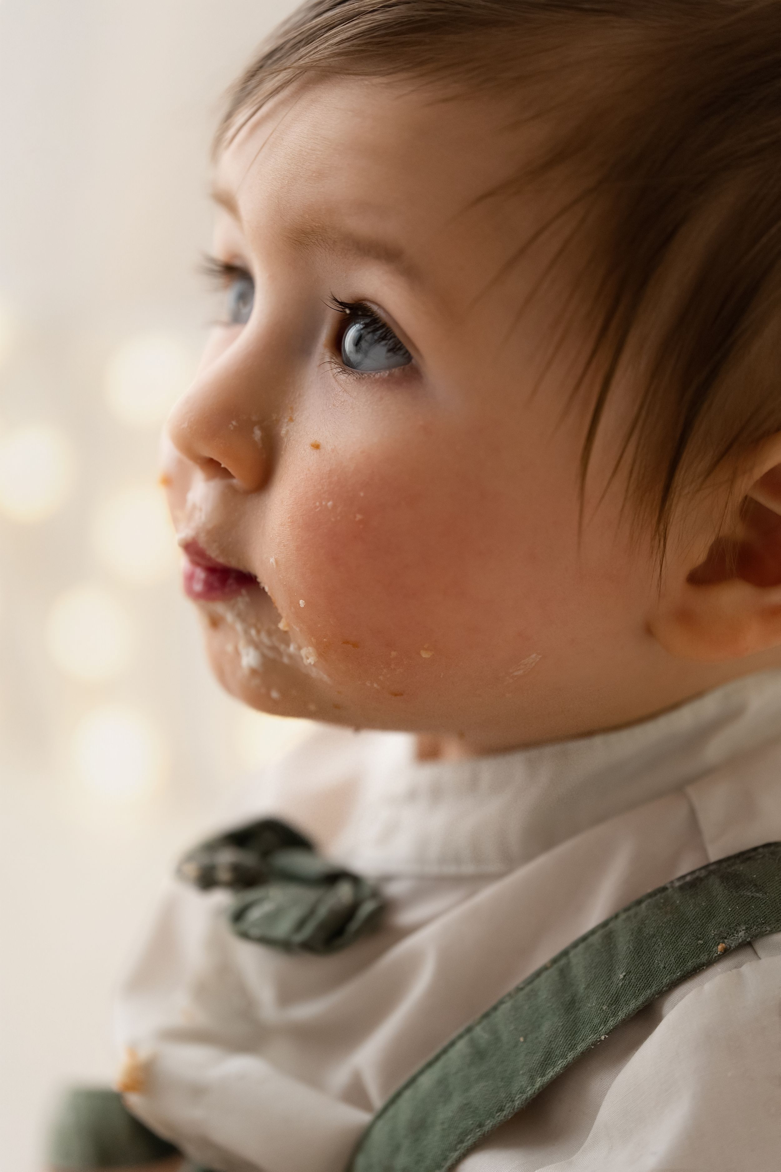 Close-up portrait of a baby boy with blue eyes and cake on his cheeks during a birthday celebration.