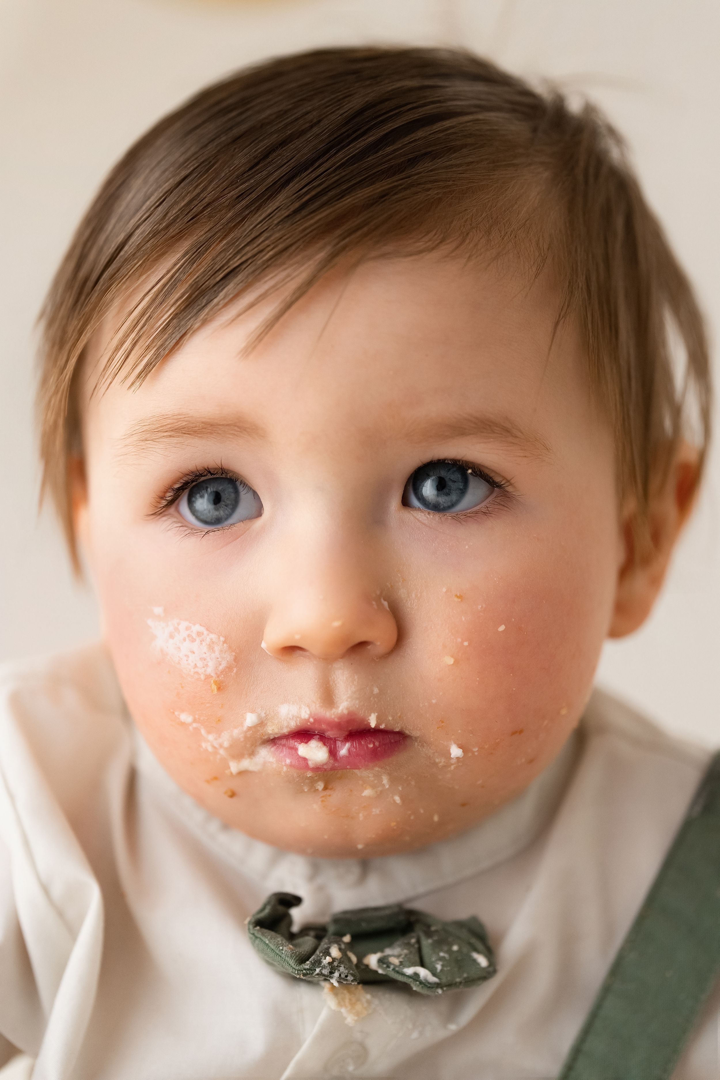 Sweet baby boy with striking blue eyes and cake frosting on his face looks at camera.