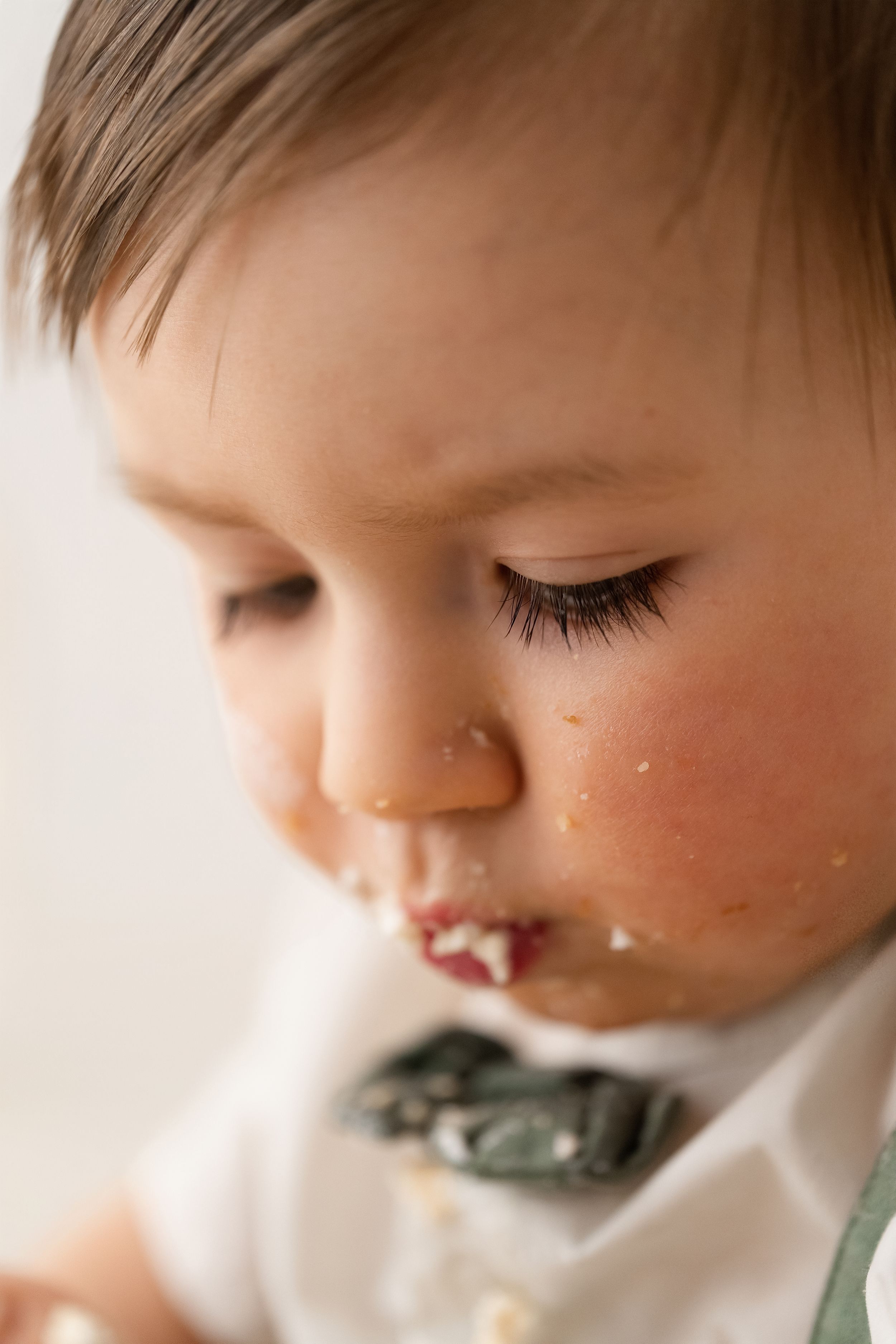 Close-up of a baby boy with long lashes and cake on his lips during a first birthday smash.