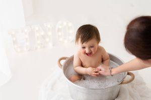 Laughing baby boy sits in a galvanized tub bath after a first birthday cake smash session.