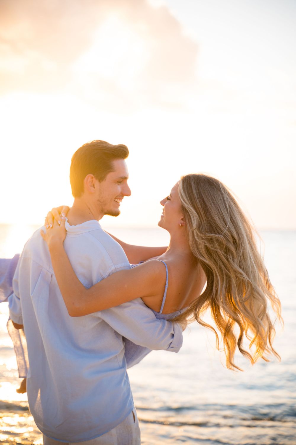 Romantic couple embracing and laughing together on a beach at sunset with golden light.