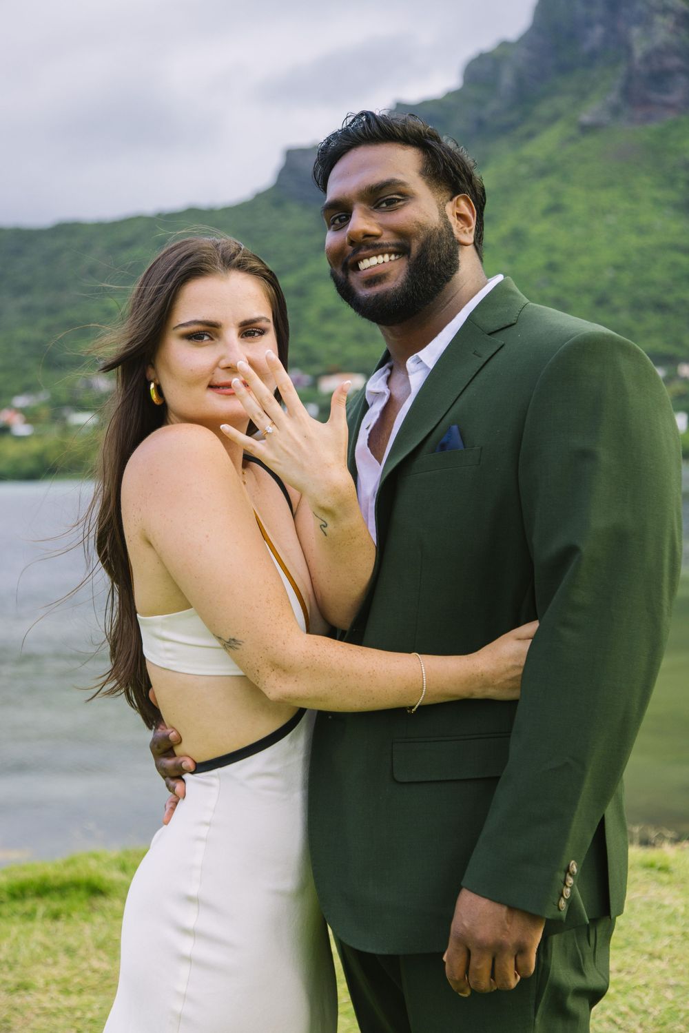 Newly engaged couple showing off ring in front of mountain landscape.
