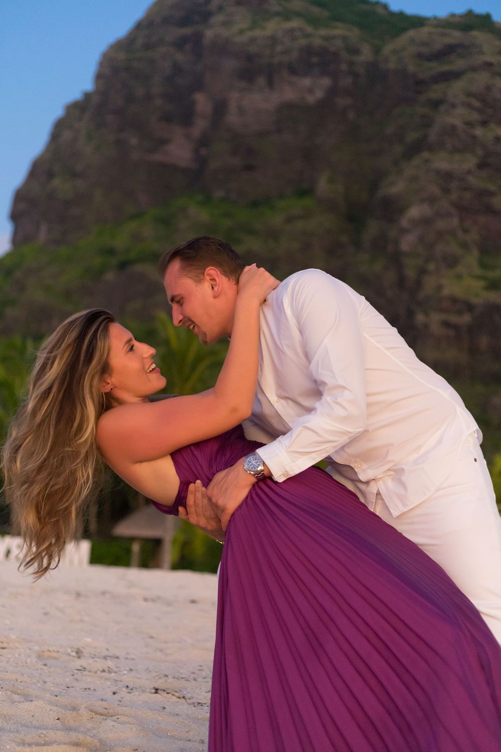 Couple in romantic dance pose on beach with dramatic mountain backdrop.
