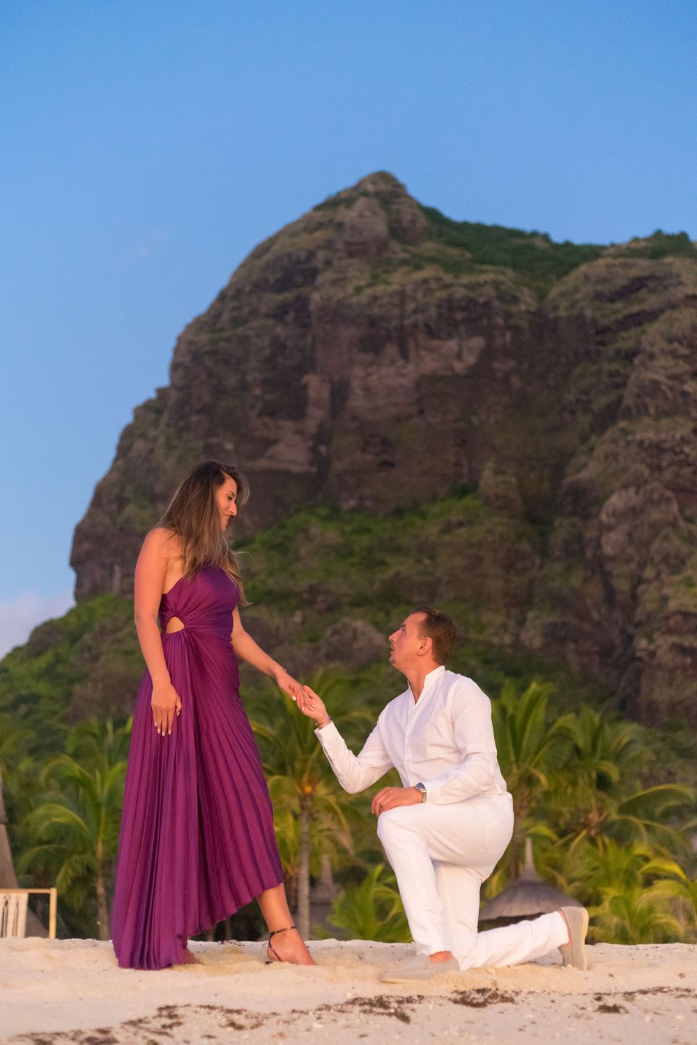 Marriage proposal scene on beach with mountain backdrop and person kneeling.