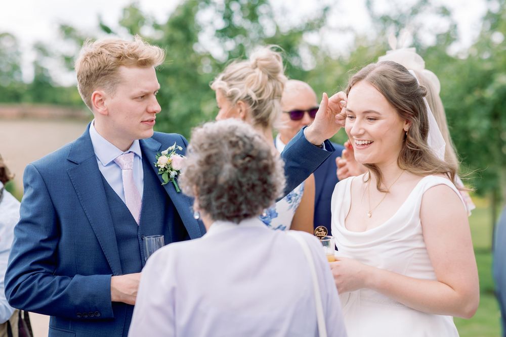 A group celebrates at an outdoor wedding reception on a sunny summer day with trees in the background.