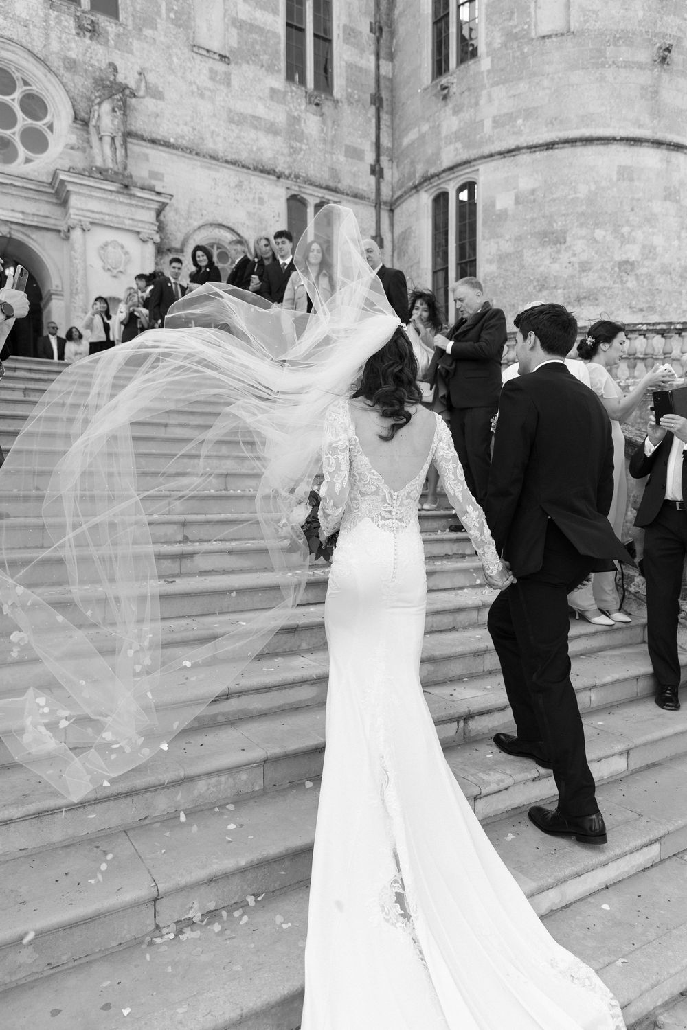 A sequence of black and white wedding photos showing a bride's veil flowing dramatically in the wind outside a stone building.