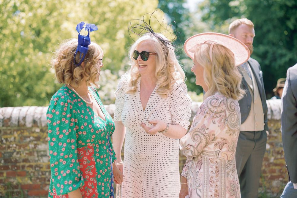 Three guests in colorful summer dresses chat and laugh together at an outdoor social gathering.