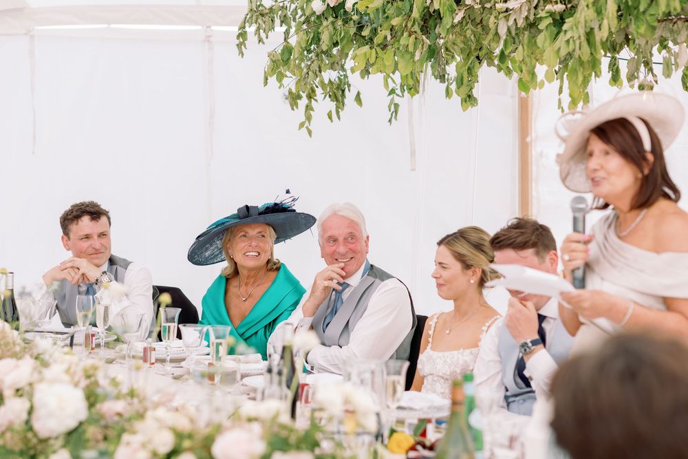 Wedding guests enjoying a sunny outdoor reception with tables decorated in white linens and floral arrangements.