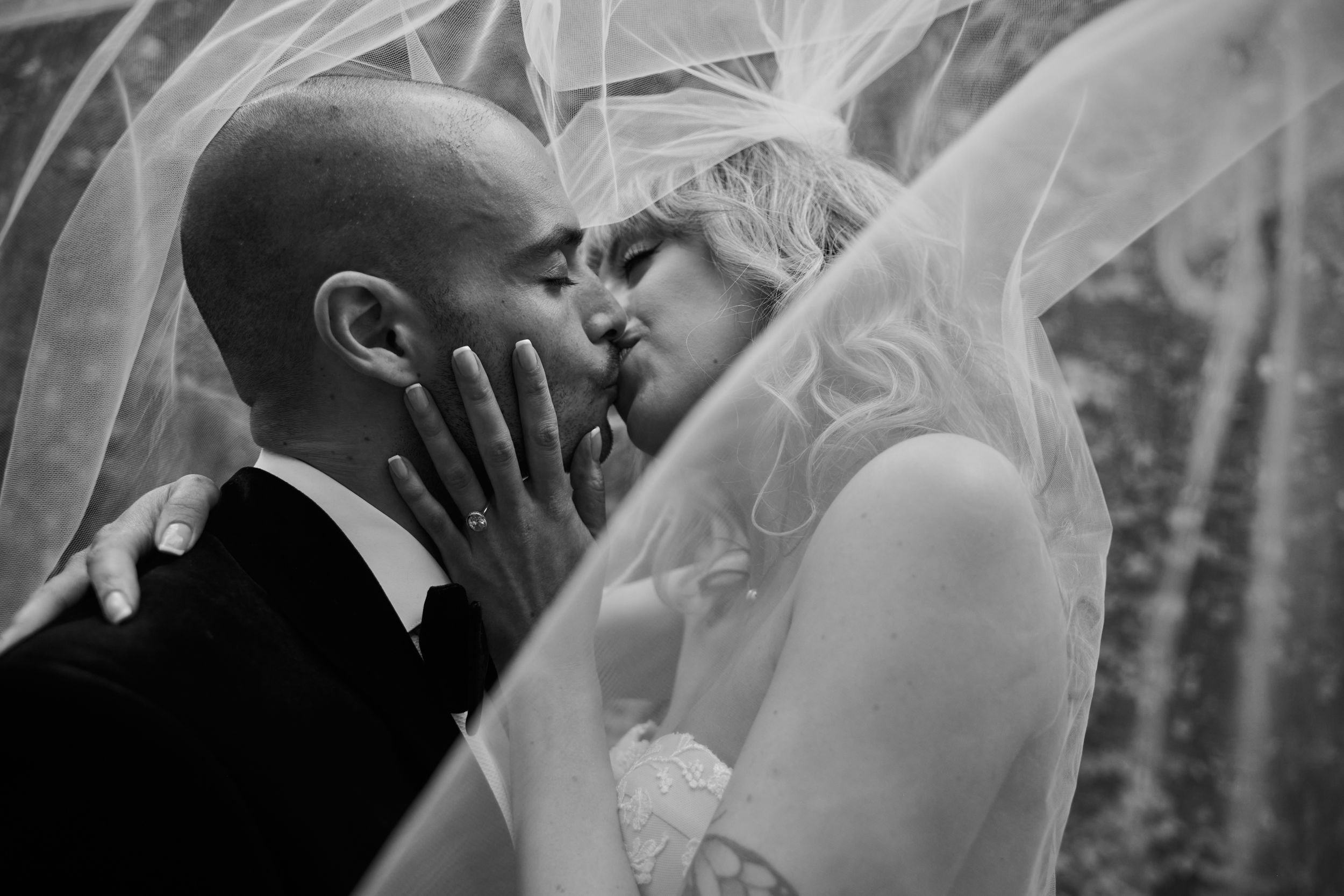 Black and white wedding portrait with couple sharing intimate moment under flowing veil.