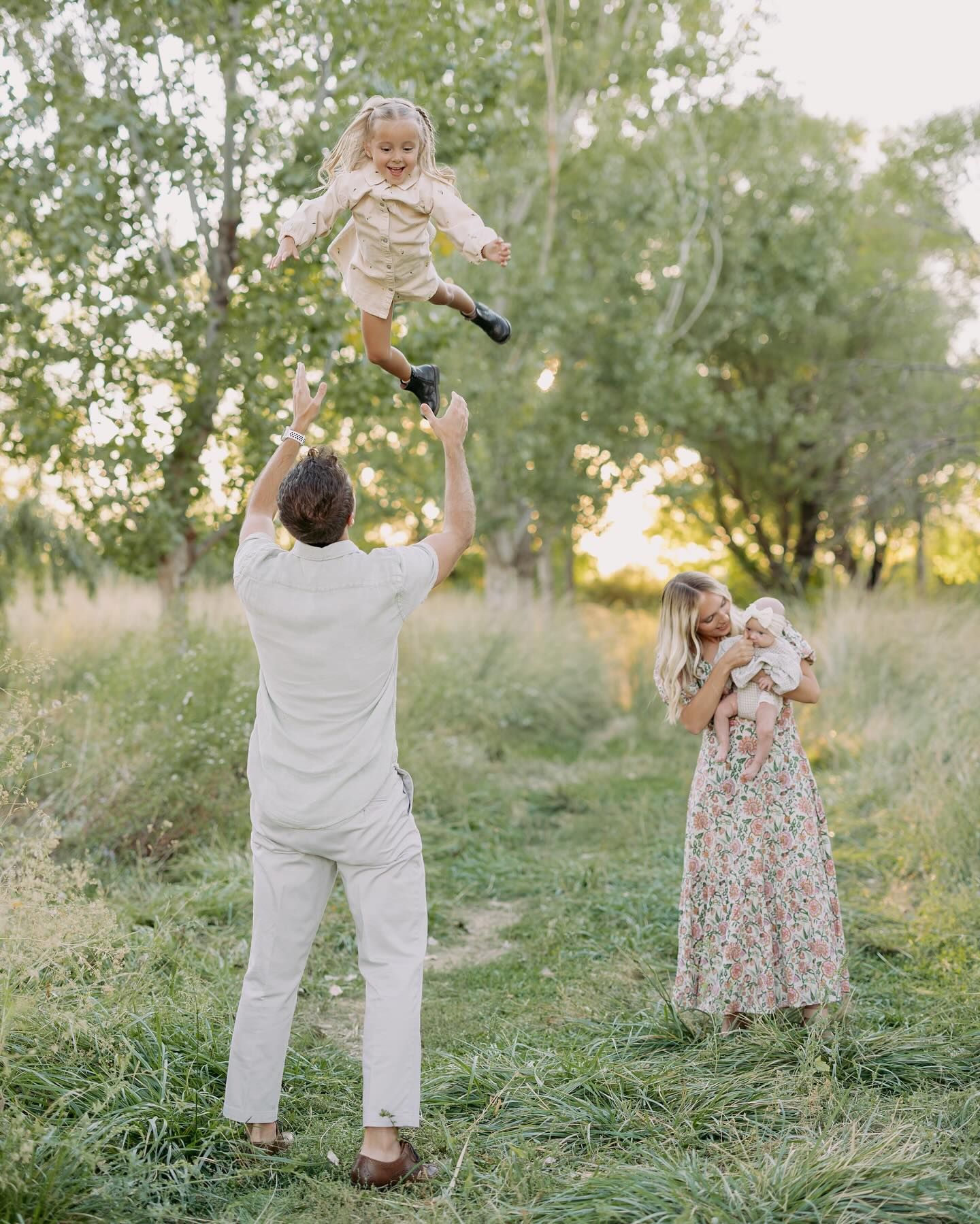 Two people playfully dance together in a grassy field at sunset with trees in the background.