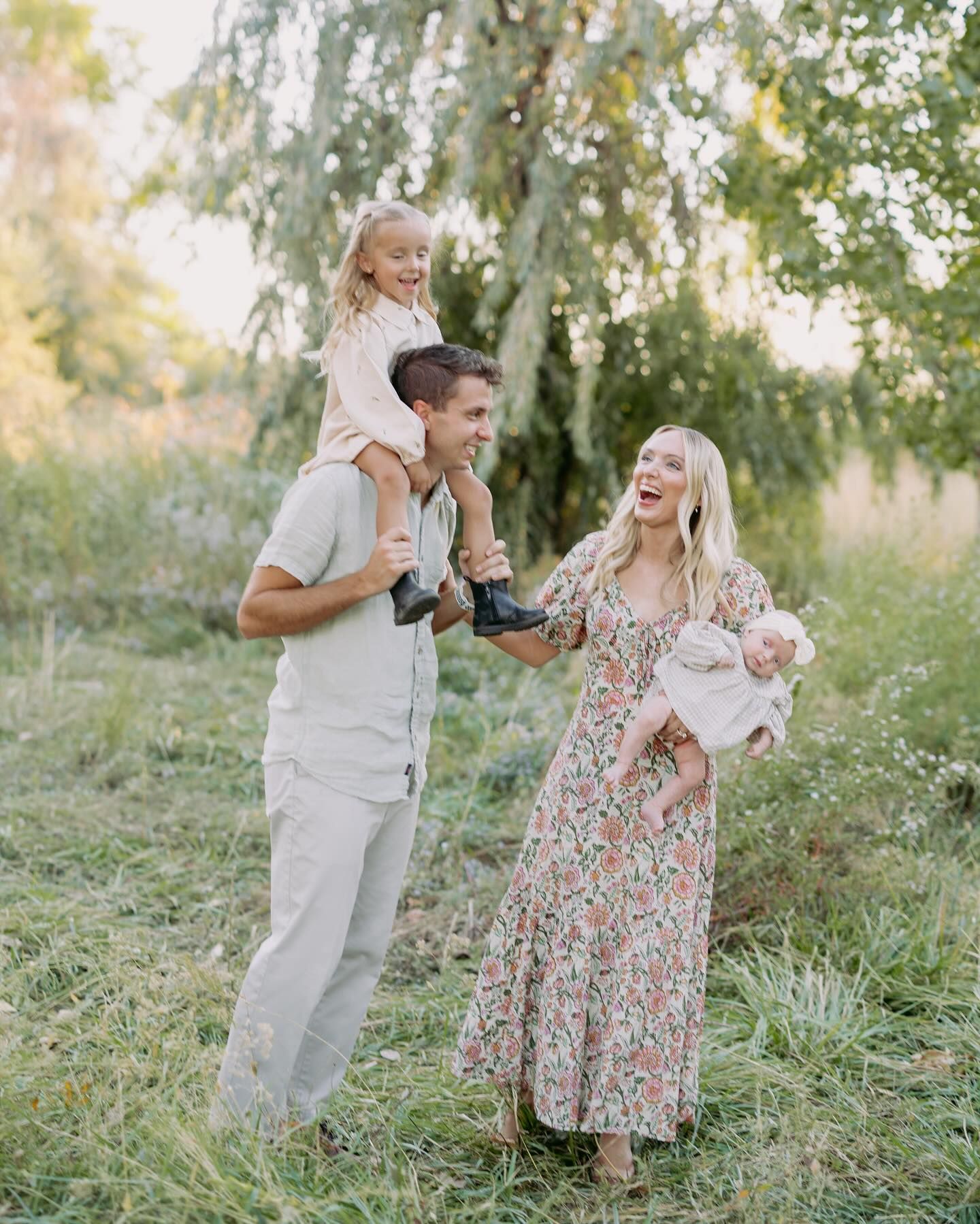Family members share joyful moments together while playing in a grassy meadow under willow trees.