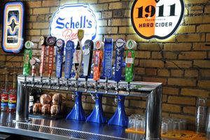 Bar interior with illuminated vintage signs and beer taps along brick wall.