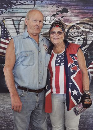 People pose in front of a rustic wooden wall decorated with American flag designs.