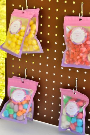 Hanging display of pink and purple candy bags with various colored treats inside.
