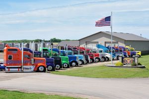A long line of colorful semi trucks parked in a row under blue skies with an American flag visible.