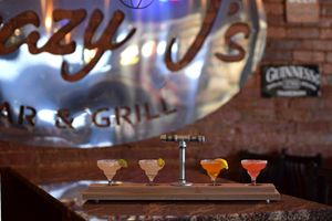 Cocktail glasses and bar equipment silhouetted against illuminated bar backdrop.