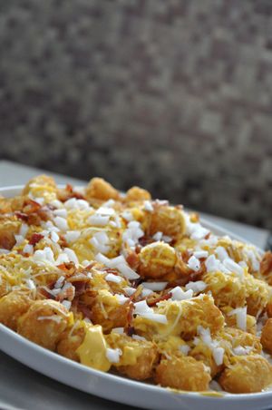 Crispy smashed potatoes topped with melted cheese and bacon bits on white platter.