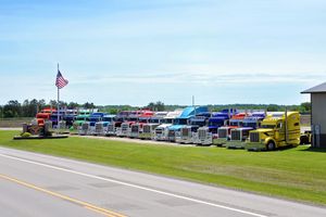 Row of colorful semi trucks parked at a truck stop with American flag under blue sky.