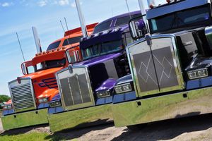 Row of colorful semi trucks lined up at a truck show with shiny chrome and custom paint jobs.