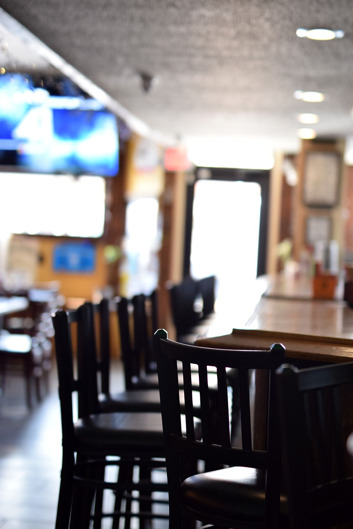 Empty restaurant interior with dark wooden chairs and tables in dim lighting.