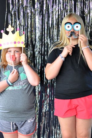 Group photo with people holding up colorful crown and eye mask props against silver backdrop.